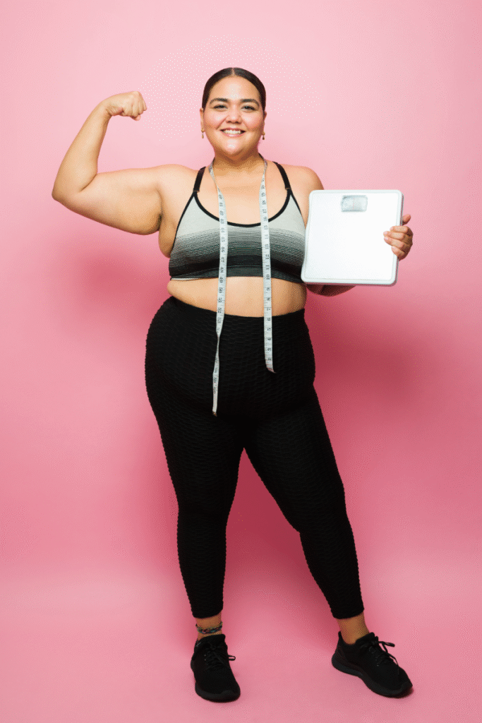 GLP-1 success - woman happy about losing weight standing with a pink background.